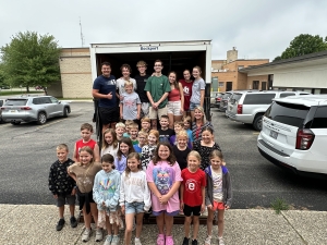 Elementary students stand in front of a loading van where they loaded up food items for FROM.