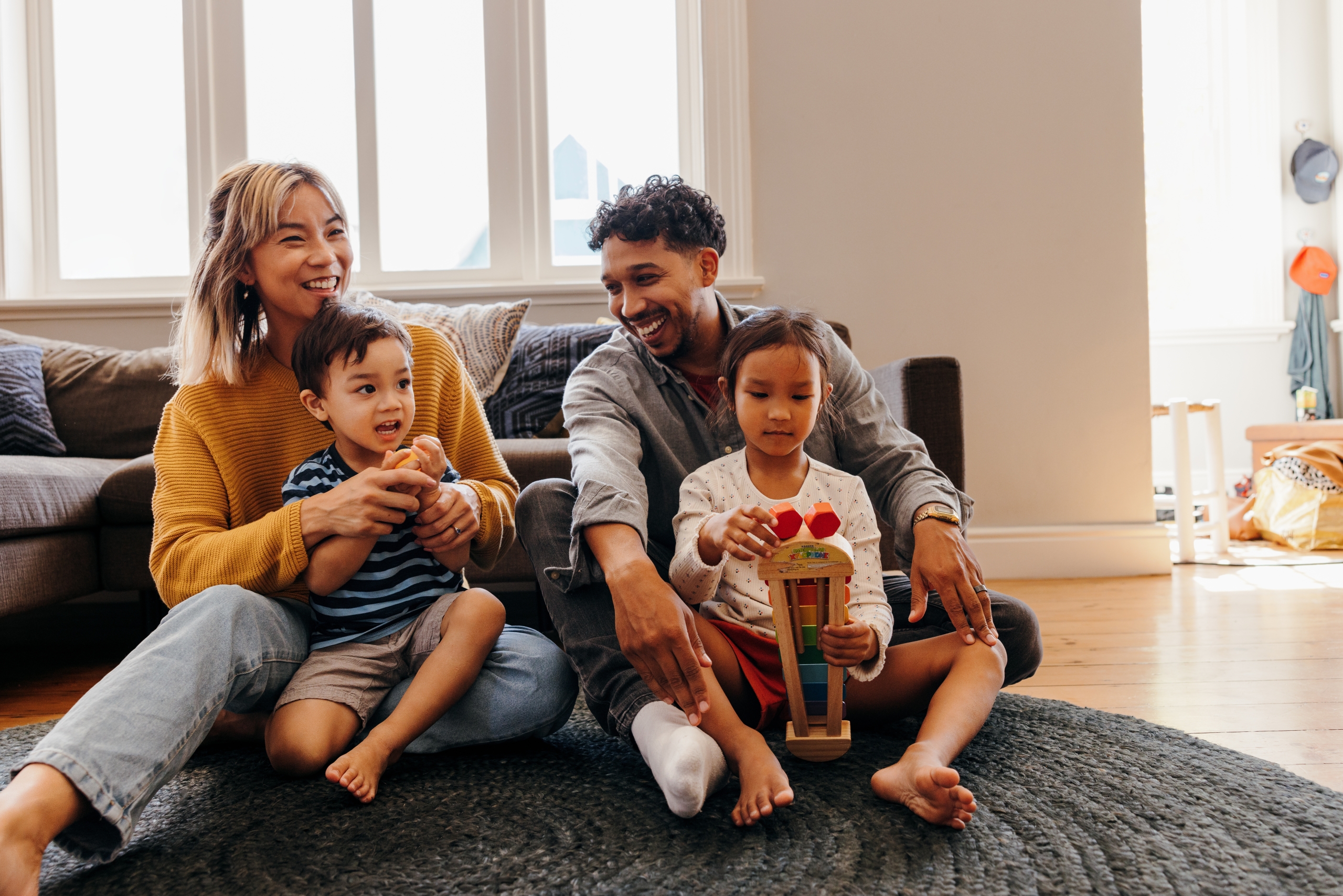 Two young parents playing with their son and daughter in the living room. Mom and dad having fun with their kids during playtime. Family of four spending some quality time together at home.